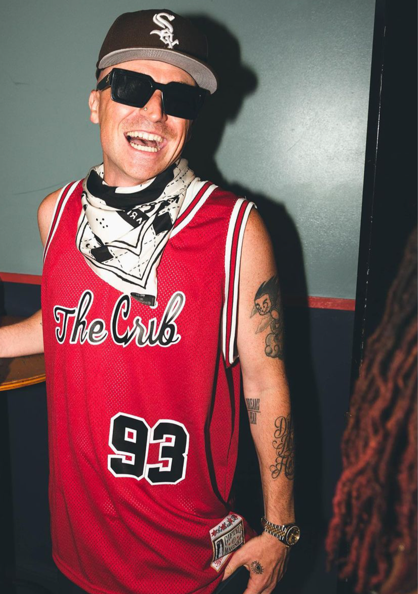 Person wearing a red 'The Crib' jersey with number 93, sunglasses, and a cap indoors.
