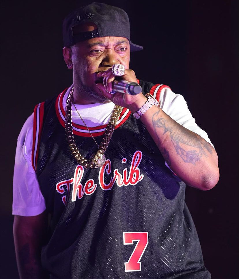 Twista wearing a 'The Crib' jersey with number 7, holding a microphone against a dark background