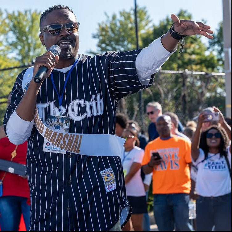 Jason Weaver in a striped shirt with 'The Crib' logo, holding a microphone outdoors.