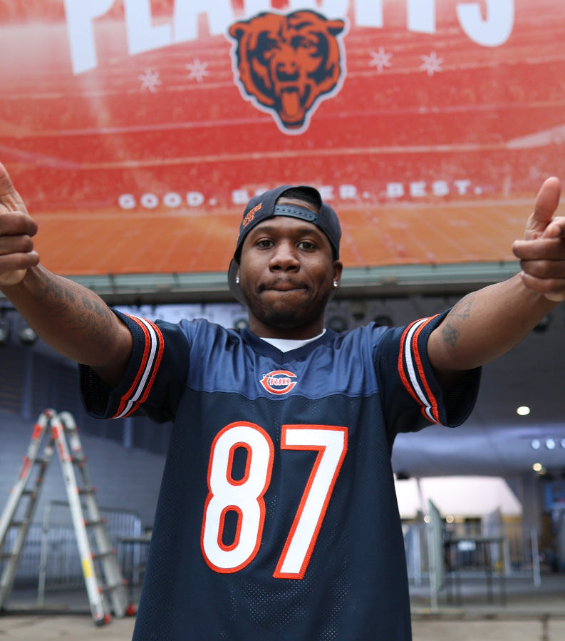 Person wearing a Chicago The Crib jersey with a large screen displaying 'Bears' in the background.