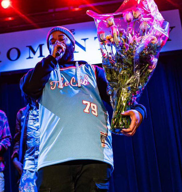 Person on stage holding flowers Wearing a The Crib jersey 
